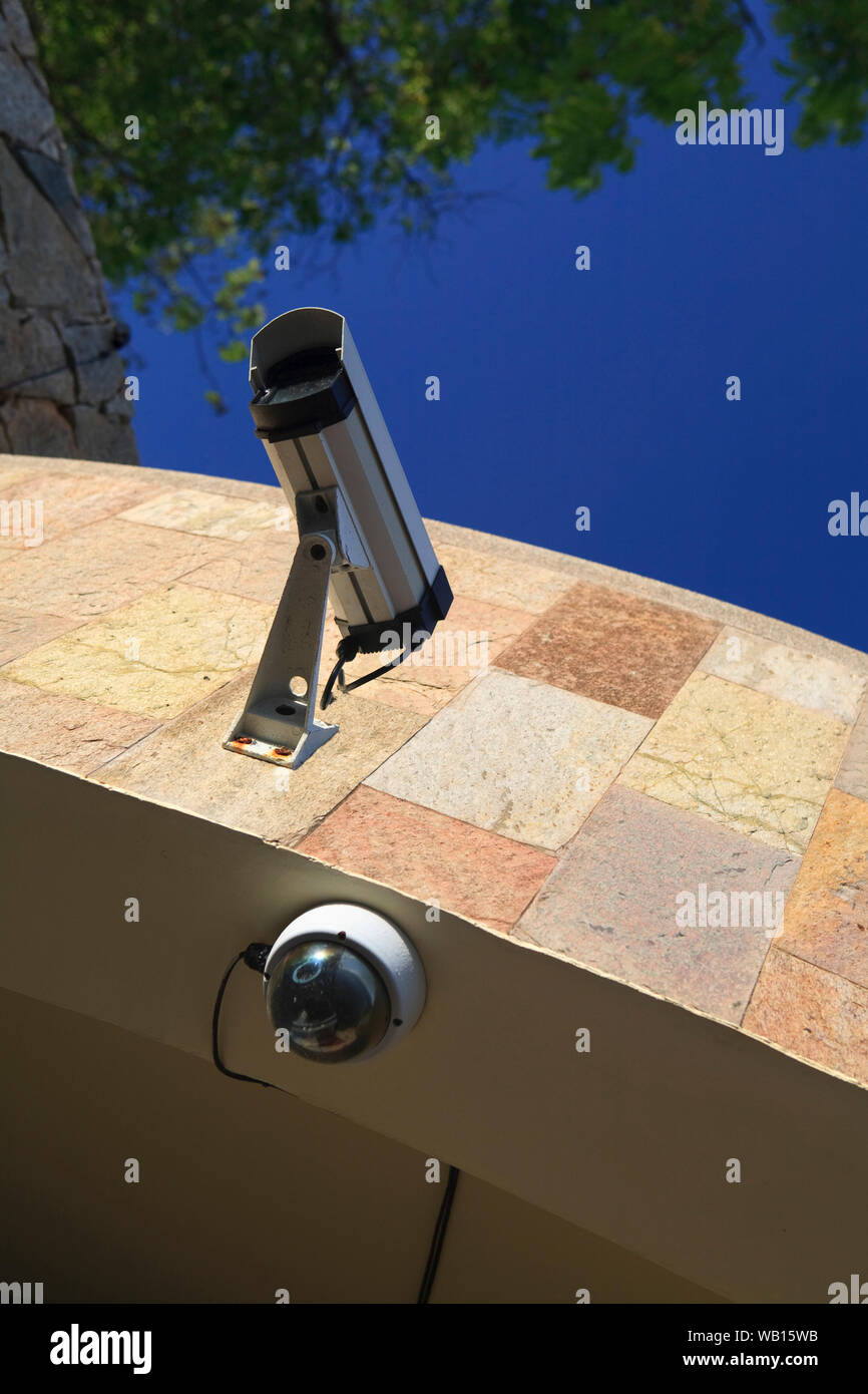 CCTV camera mounted on an exterior wall of a building, against a blue sky. Stock Photo