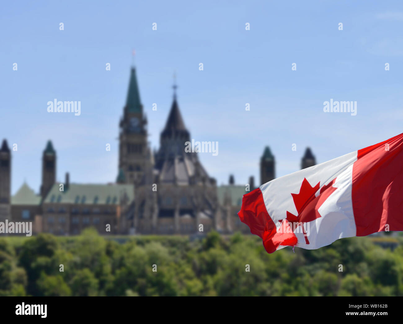 Picture of Parliament Hill and the Peace Tower in Ottawa, Ontario, Canada.  Canadian flag in the foreground, with the building blurred for effect Stock Photo