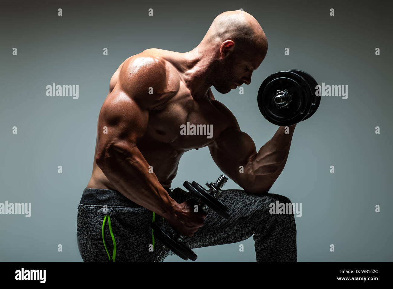 Strong young man bodybuilder performing exercise for biceps with heavy dumbbell in both hands Concept Artistic Gym Life Style Stock Photo