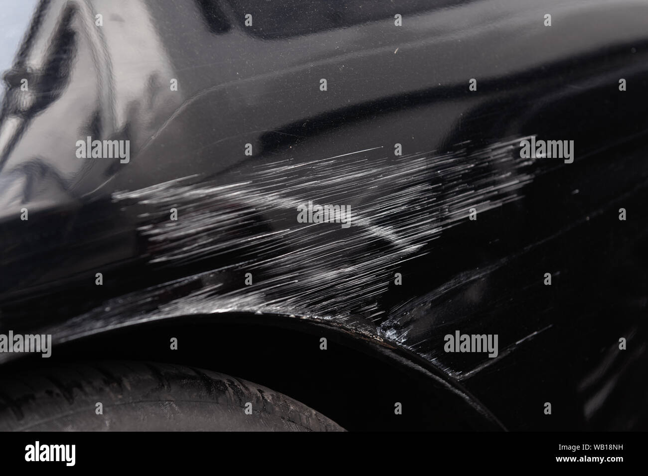 Damaged car body after a crash accident. Black vehicle wheel arch closeup. Scratches and dents