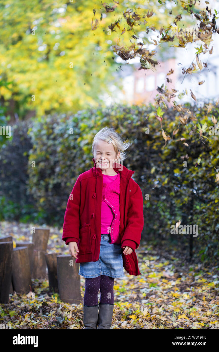 Portrait of grinning little girl throwing leaves in the air in autumn Stock Photo