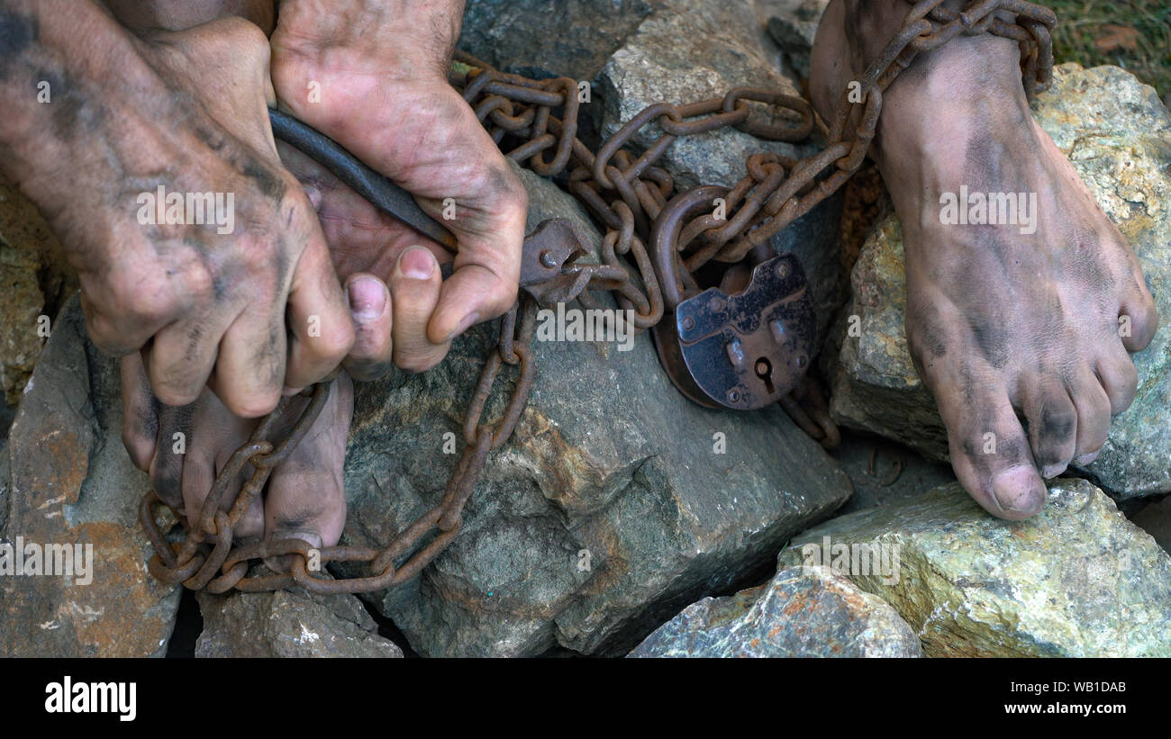Hands and feet of a slave entangled in iron chains. An attempt to break free from slavery. The symbol of slave labor. Hands in chains Stock Photo