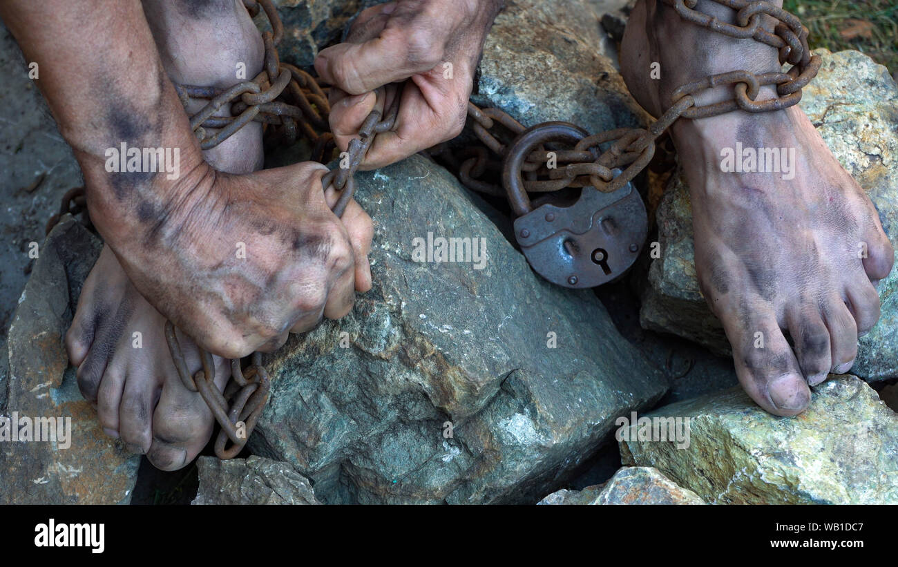 Hands and feet of a slave entangled in iron chains. An attempt to break