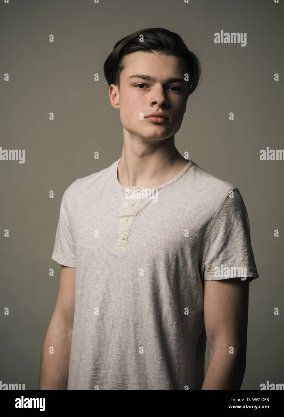 Teenage boy in white T-shirt isolated on gray background. Portrait of confident young man with long hair, eagerness of youth. Stock Photo