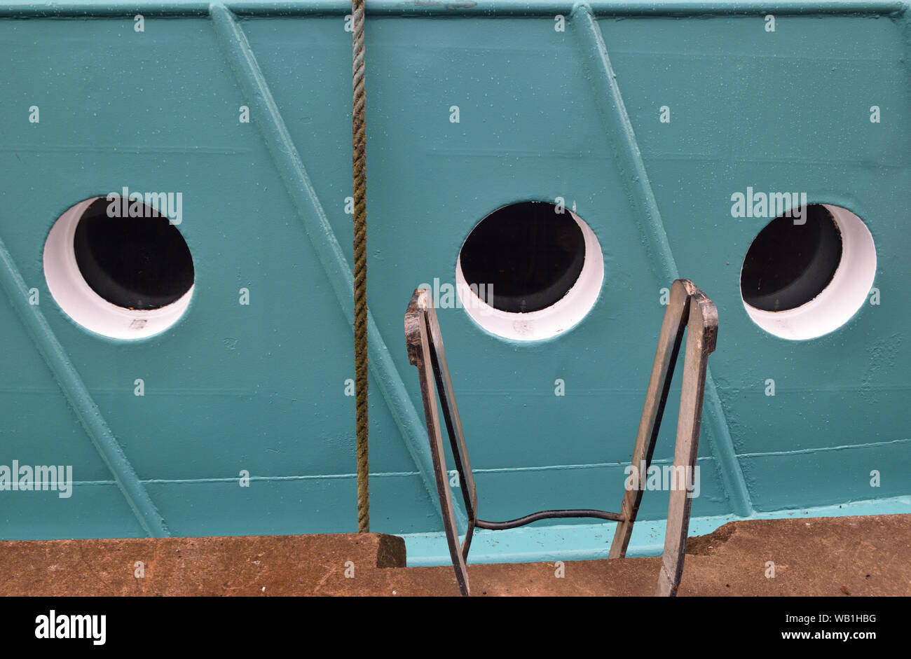 3 portholes in the blue painted hull of a ship moored in harbour by ...