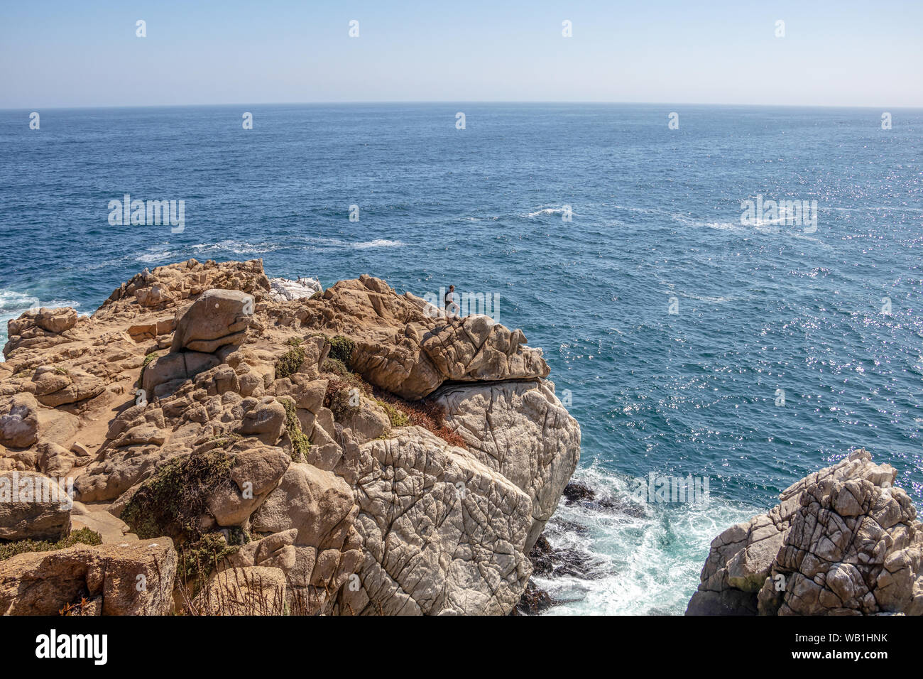 Young male traveler at rock formation rising out of cold Pacific ocean waters Stock Photo