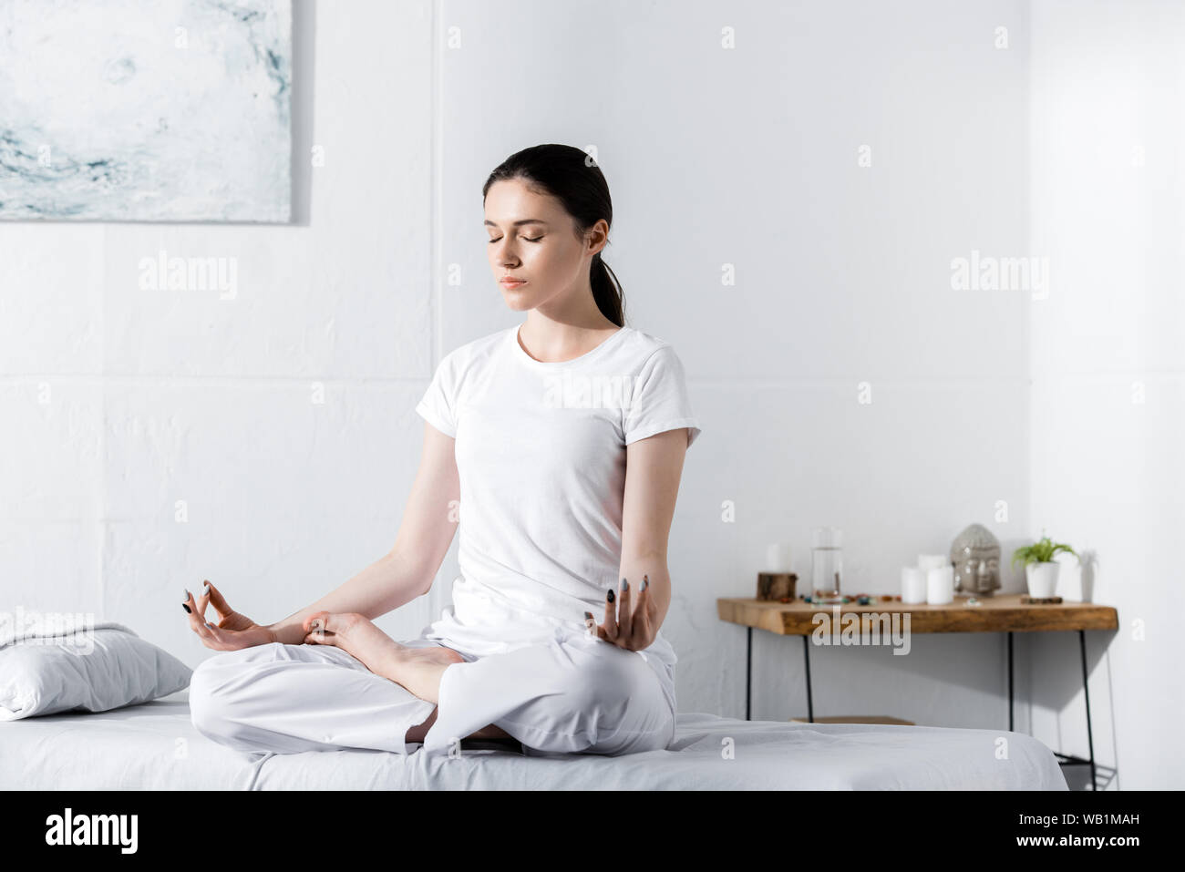 young woman sitting in lotus pose with closed eyes on massage table ...