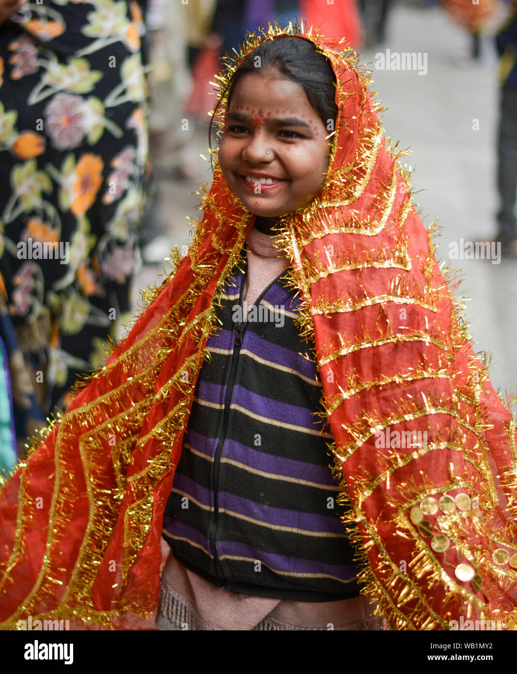 Girl child beggar smiling at camera in colorful religious dress. Stock Photo