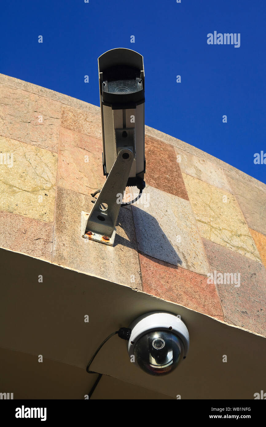CCTV camera mounted on an exterior wall of a building, against a blue sky. Stock Photo