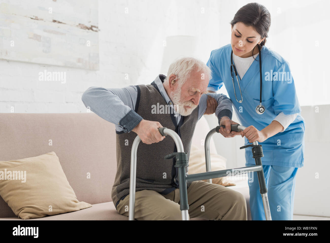 Doctor helping to retired man, getting up from sofa Stock Photo