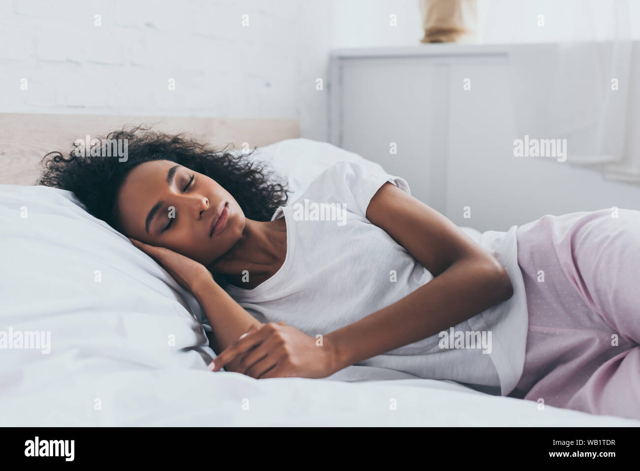 pretty african american woman in pajamas sleeping on white bedding
