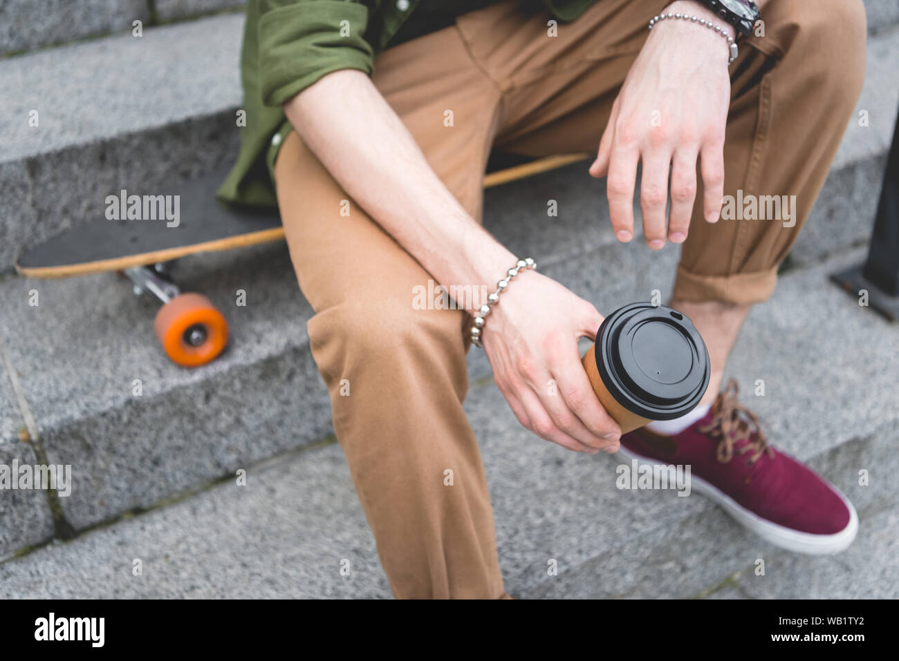 cropped view of man with paper cup in hand sitting on stairs Stock ...