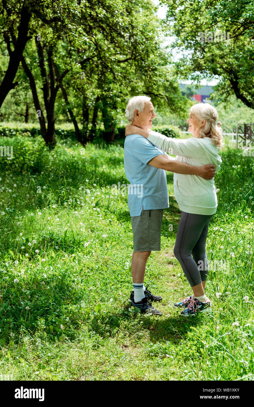 smiling retired man hugging happy senior wife while standing in green park Stock Photo