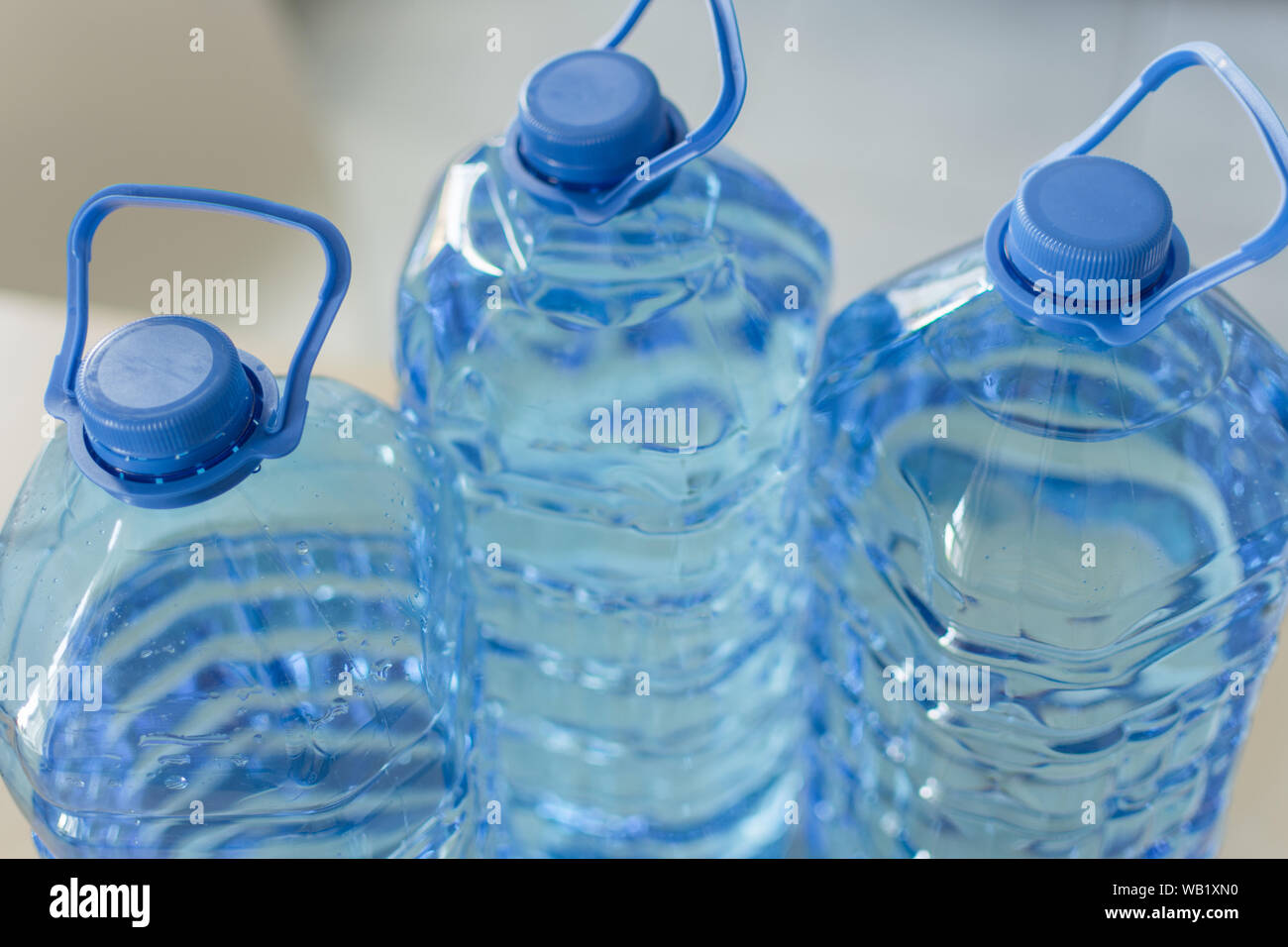 https://c8.alamy.com/comp/WB1XN0/big-plastic-bottle-with-water-on-the-table-over-bright-kitchen-backgroung-bottle-of-clear-transarent-water-in-a-blue-color-cap-and-handle-closeup-WB1XN0.jpg
