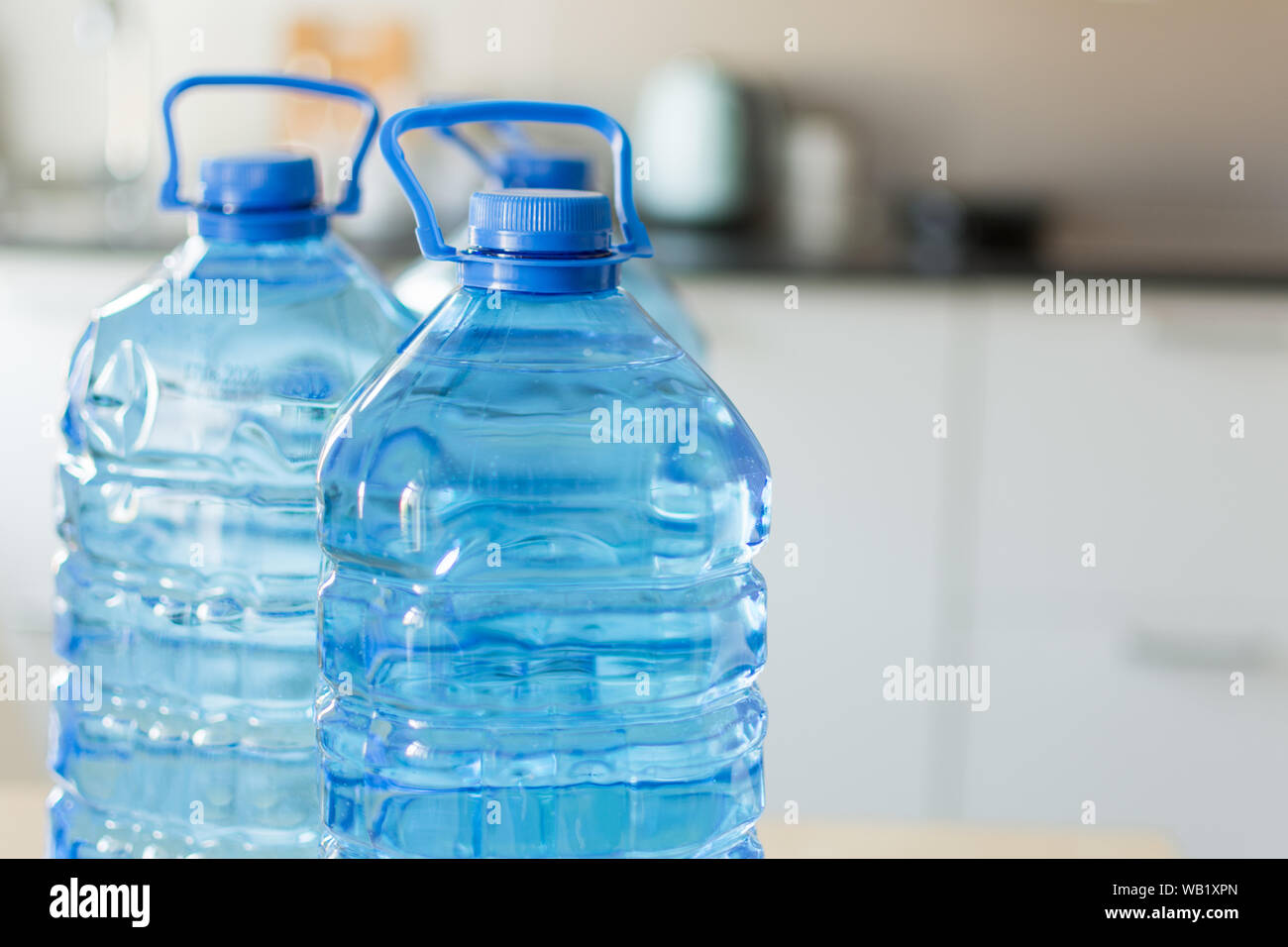 https://c8.alamy.com/comp/WB1XPN/big-plastic-bottle-with-water-on-the-table-over-bright-kitchen-backgroung-bottle-of-clear-transarent-water-in-a-blue-color-cap-and-handle-closeup-WB1XPN.jpg