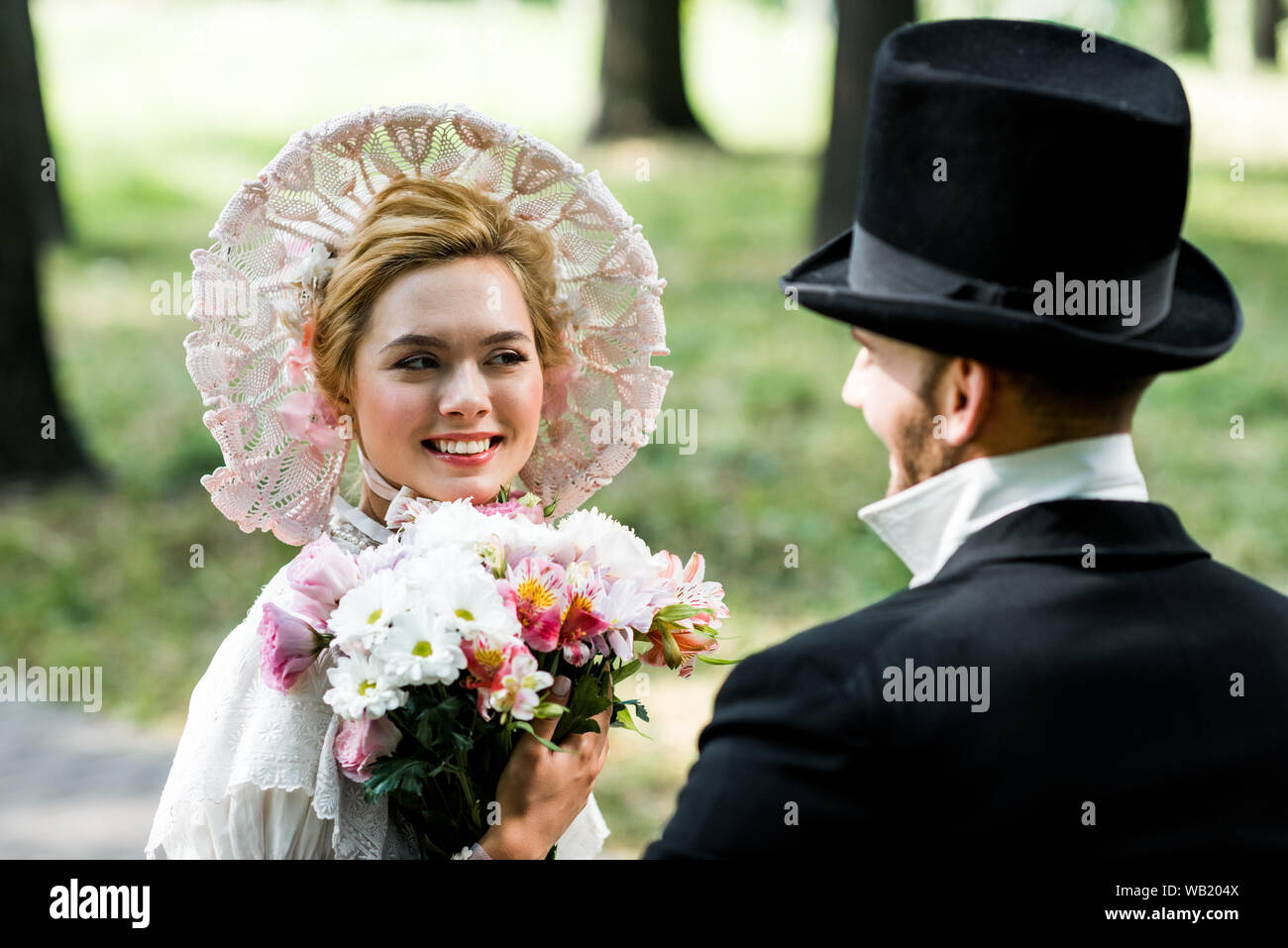 selective focus of happy victorian woman holding flowers and looking at gentleman Stock Photo