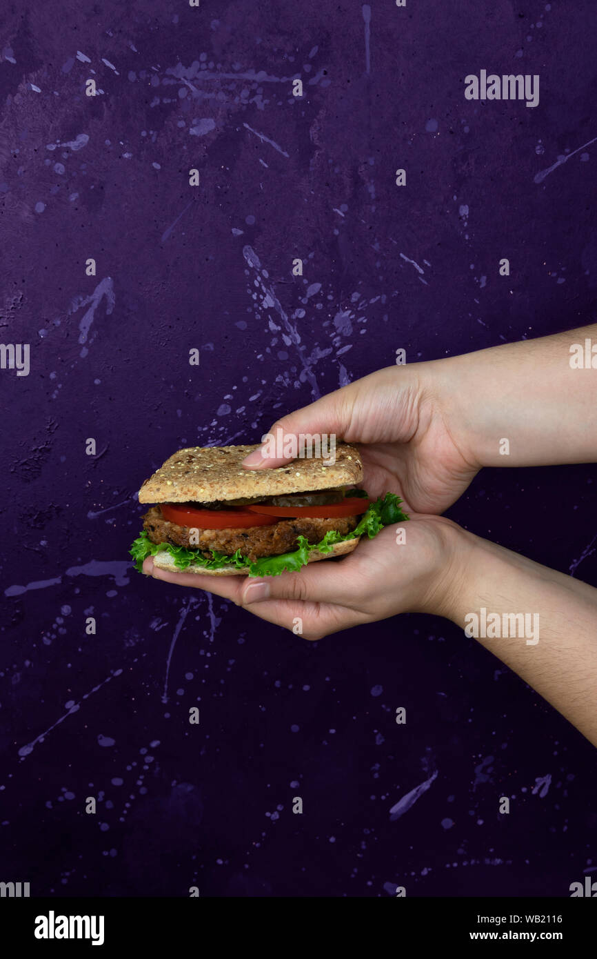 A young girls hands holding a delicious healthy vegan burger on purple modern background Stock Photo