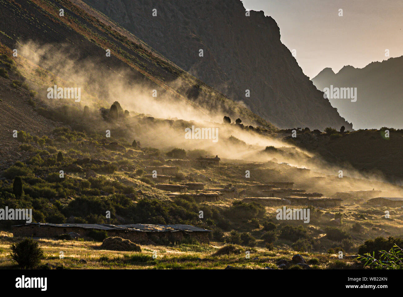 Dust rises above the mud houses of the mountain village of Sarytag, Tajikistan, stirred up by passing vehicles in the low evening light. Stock Photo