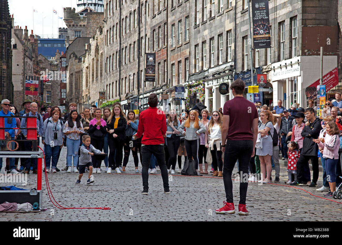 Royal Mile, Edinburgh, Scotland, UK. 23rd August 2019. Juggler on the Lawnmarket teases a young volunteer who is attempting to catch one of the juggling balls. Stock Photo