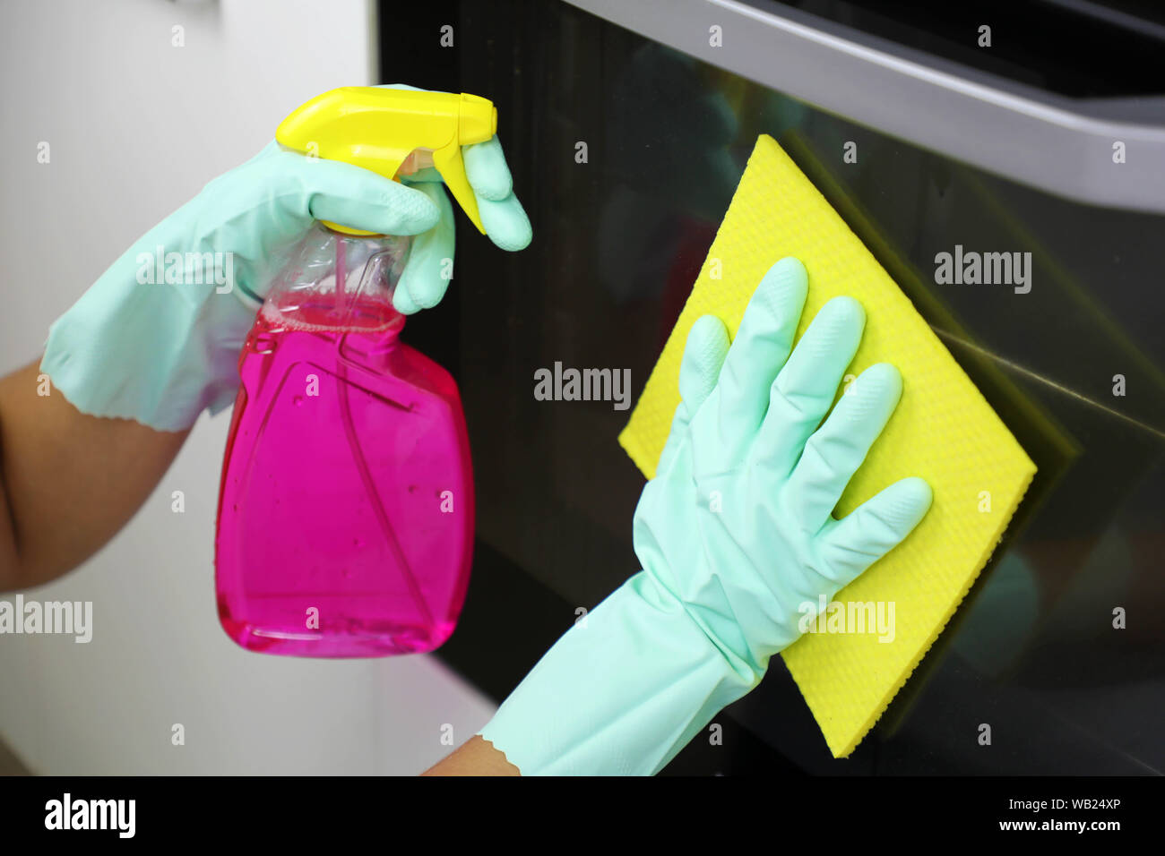 Close up of female hands with protective gloves cleaning oven door. Girl polishing kitchen. People, housework, cleaning concept. Stock Photo