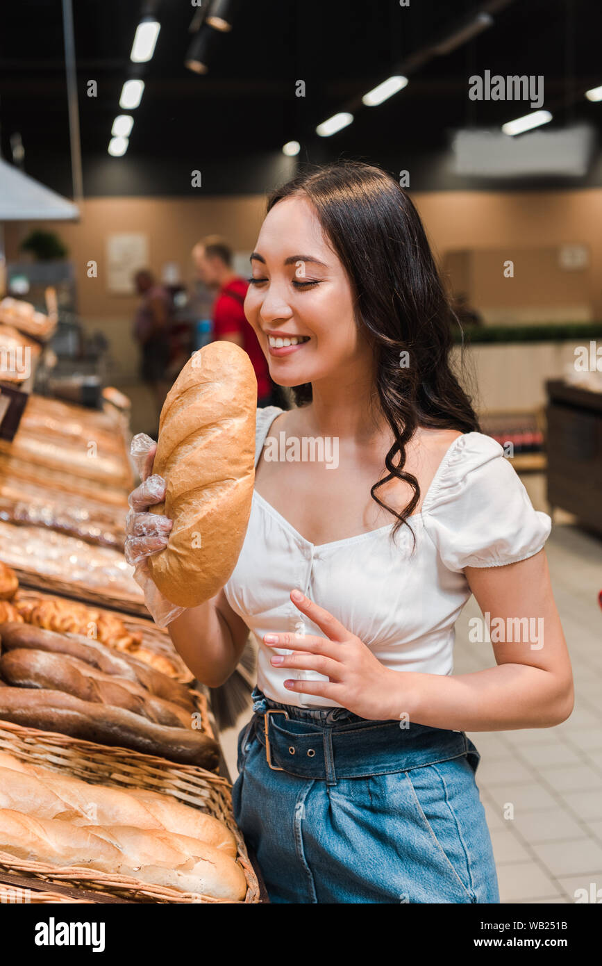 happy asian woman smiling while smelling bread in supermarket Stock