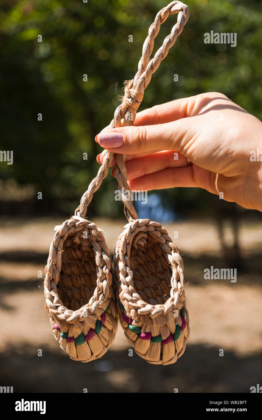 Straw baby souvenir shoes in women's hands on the park's summer park. Two straws shoe. Mascot