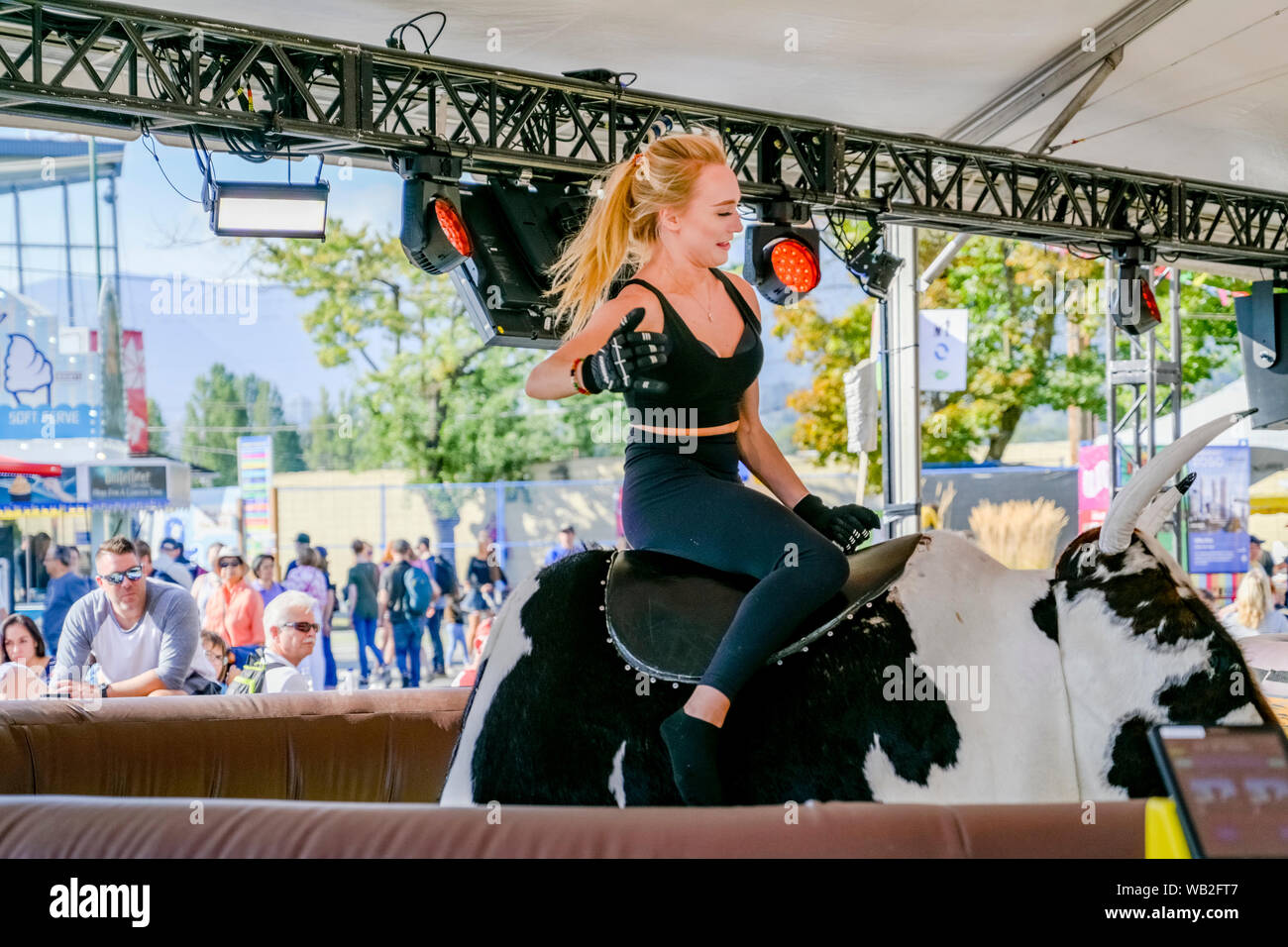 Women, riding, mechanical bull at carnival, midway, amusement park Stock Photo