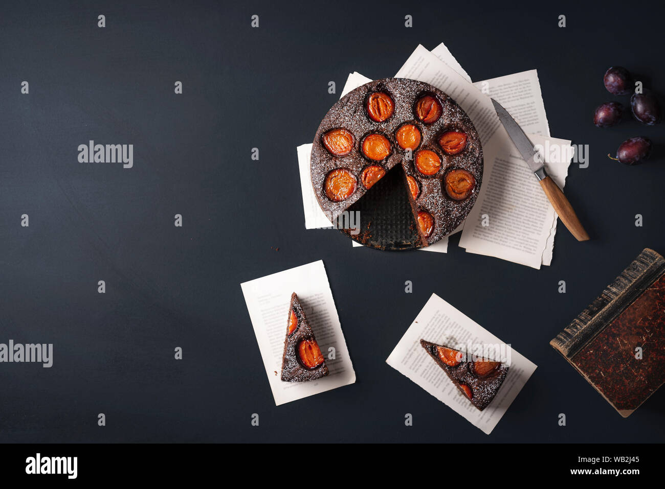 Plums dessert with chocolate and two slices on old books pages. Above view with autumn sweet food. Relaxing time frame. Flat lay with copy space. Stock Photo