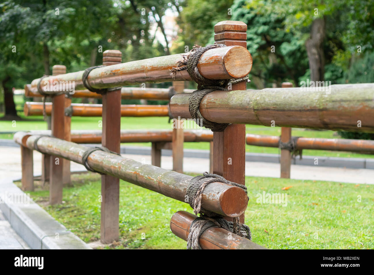 A wooden log fence fixed with a rope in a park next to an asphalt path with  a concrete curb. Against the background of trees in summer Stock Photo -  Alamy