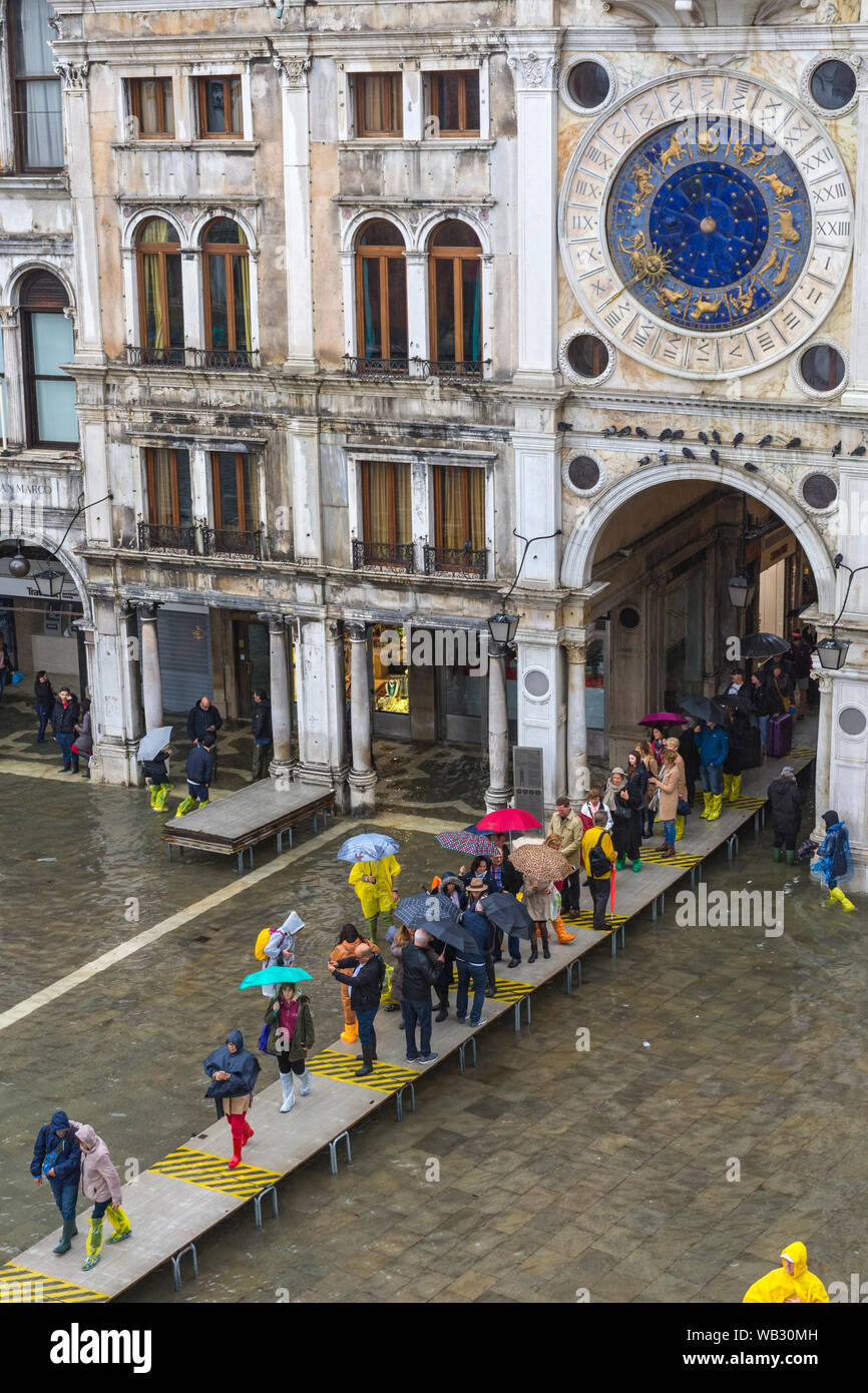 People on elevated platforms at the archway to the Merceria during an Acqua alta (high water) event, Saint Mark's Square, Venice, Italy Stock Photo