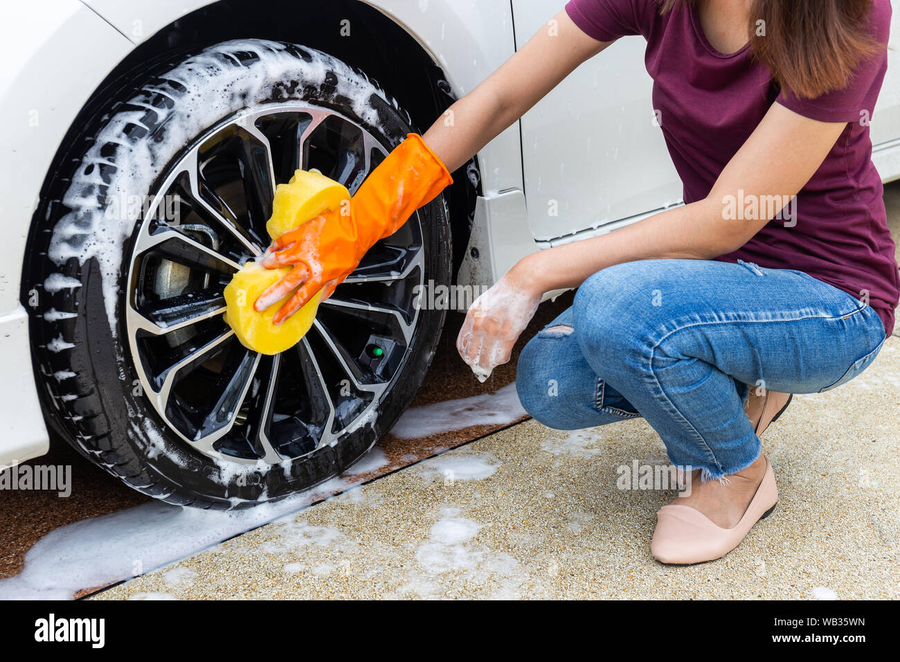 Woman hand wearing orange gloves with yellow sponge washing wheel modern car or cleaning automobile. Car wash concept Stock Photo