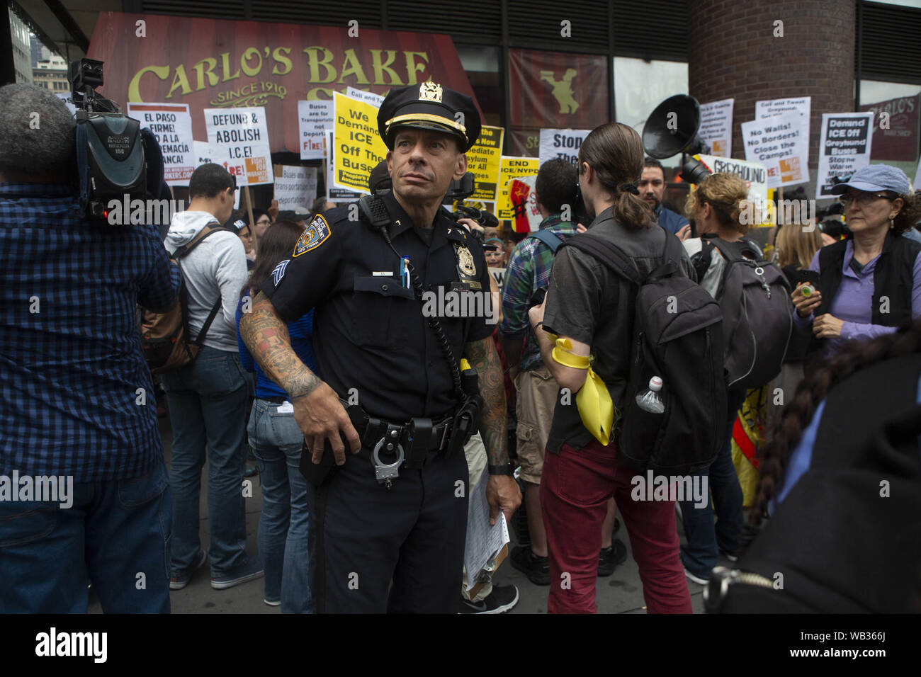 August 23, 2019: A New York Police officer stands in front of a protest against Greyhound Corporation and ICE (Immigration Customs and Enforcement) at the Port Authority Bus Terminal on 42nd and 8th Avenue in New York, New York. About 100 activists from a coalition of groups including FIRE (Fight For Immigrant Refugees Everywhere) protested Greyhound allowing ICE agents to board their busses 'searching for migrants,'' officials said. Credit: Brian Branch Price/ZUMA Wire/Alamy Live News Stock Photo