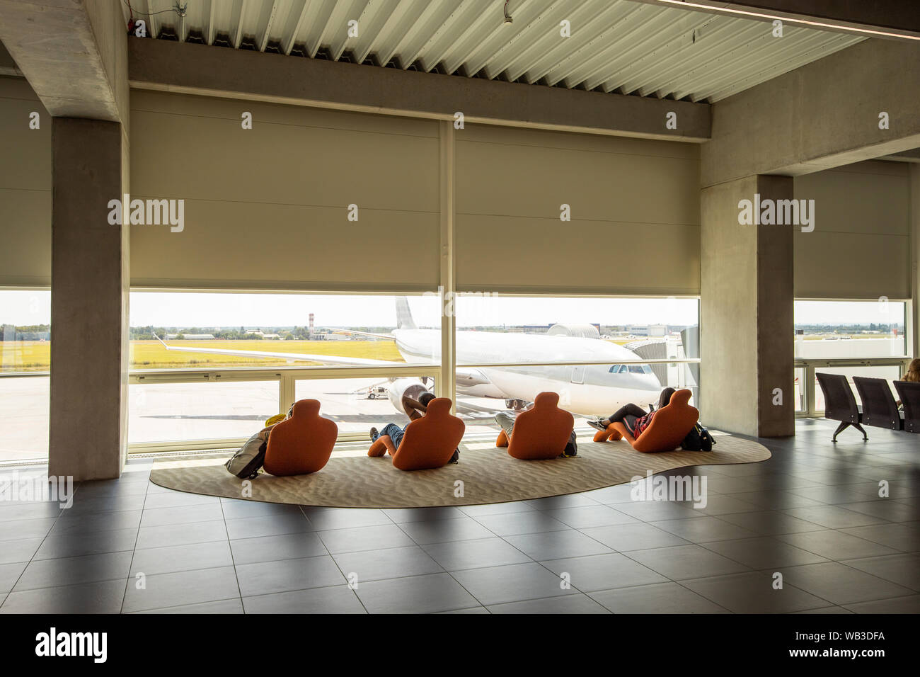 Travelers relaxing on lounge chairs, watching at airport window. Unrecognizable people looking at airplane, waiting. Airport airplane waiting Stock Photo