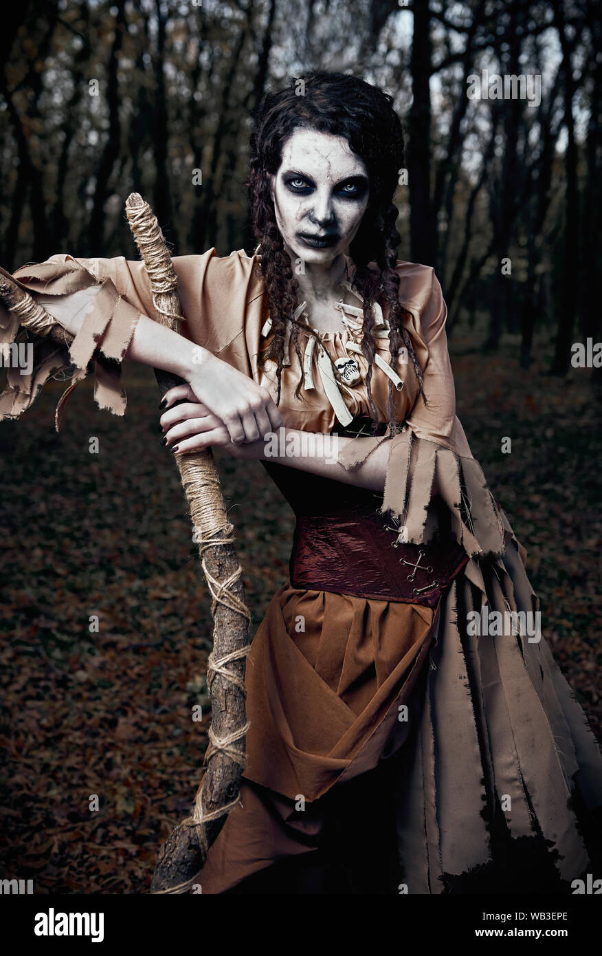 Halloween theme: wicked scary voodoo witch with staff. Portrait of the evil sorceress in dark grove. Zombie woman (undead) Stock Photo