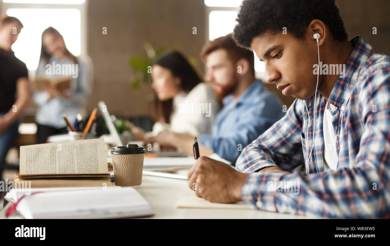 African-american guy preparing for exam, taking notes in library Stock Photo