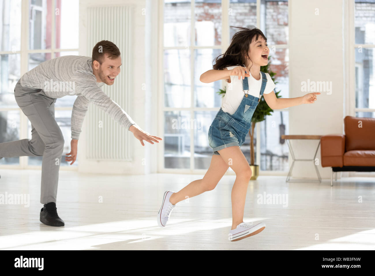 Cute child daughter running from dad playing tag game together Stock Photo