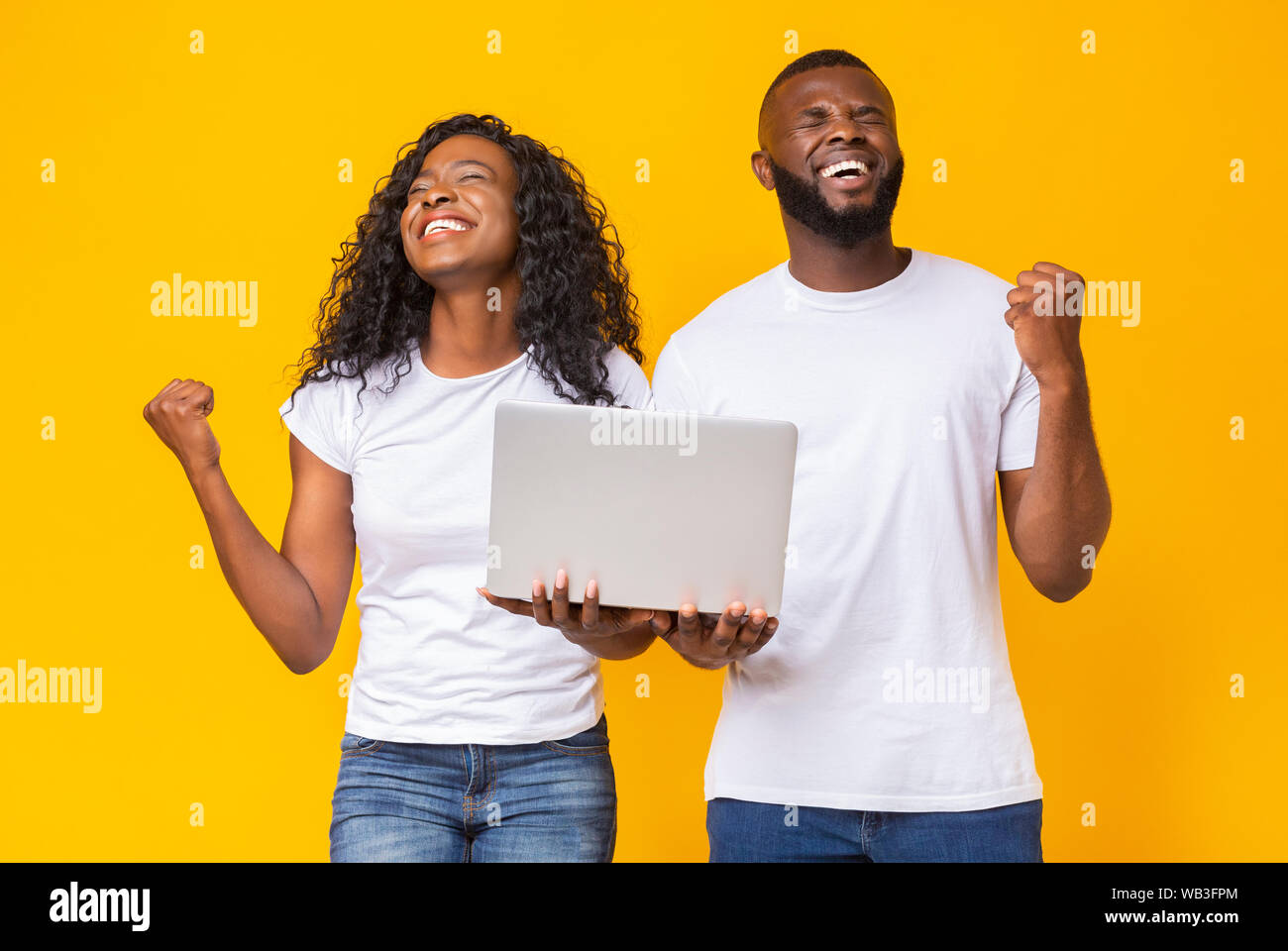 Extremely happy afro couple with closed eyes celebrating win Stock Photo