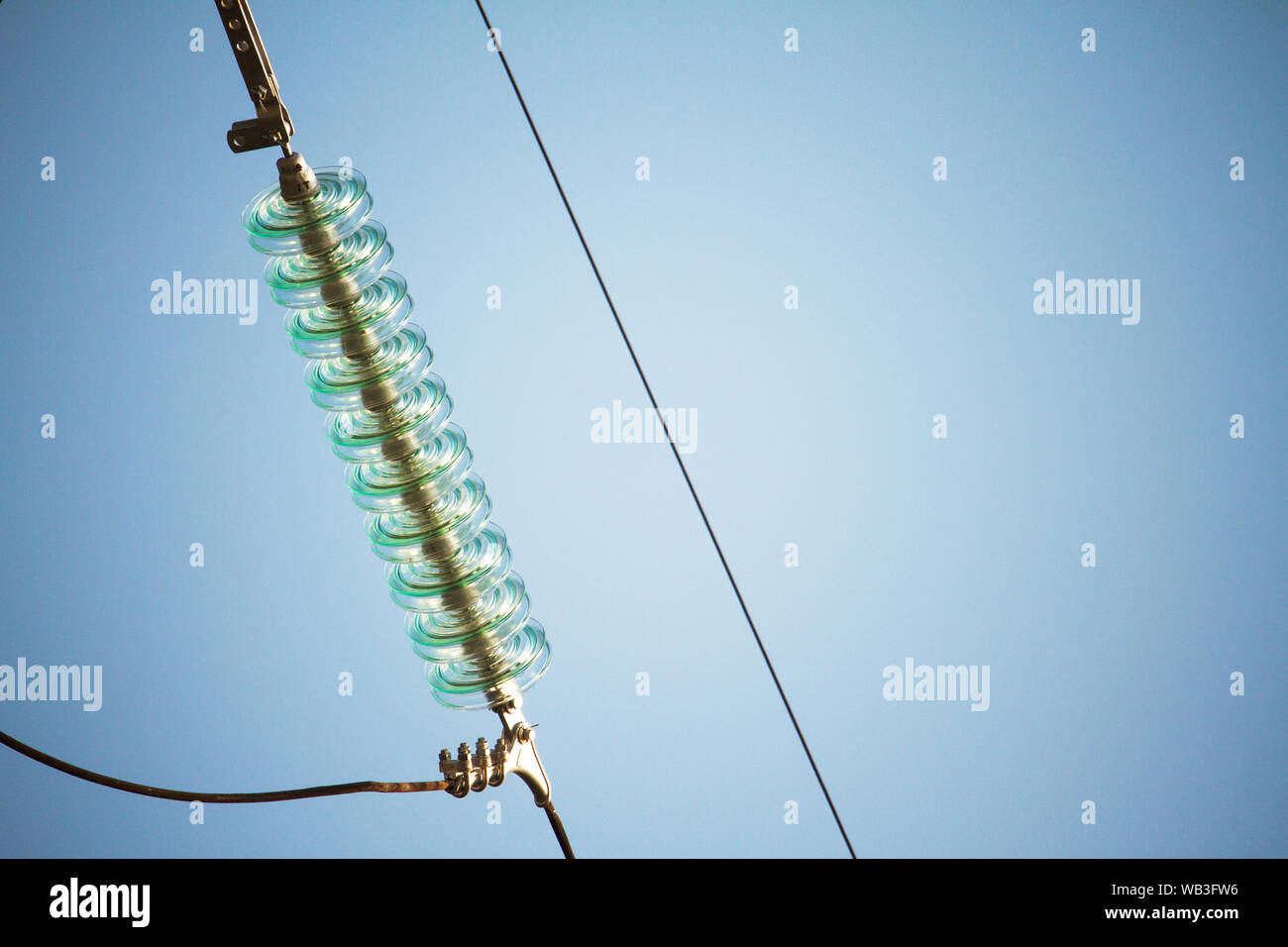 Close up bottom view of insulators on high-voltage wires on a power tower against a blue sky Stock Photo