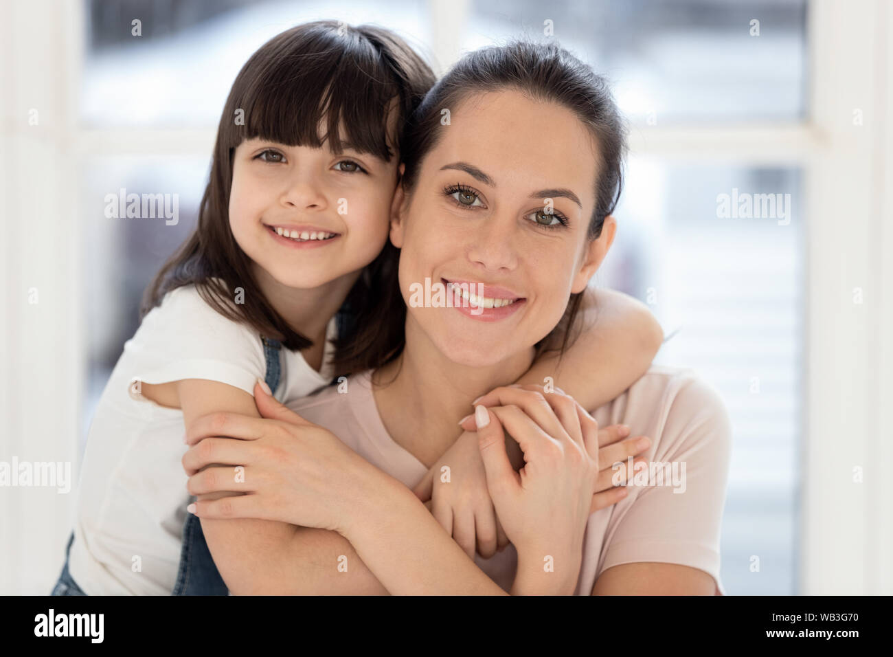 Happy kid daughter embracing mother bonding together looking at camera
