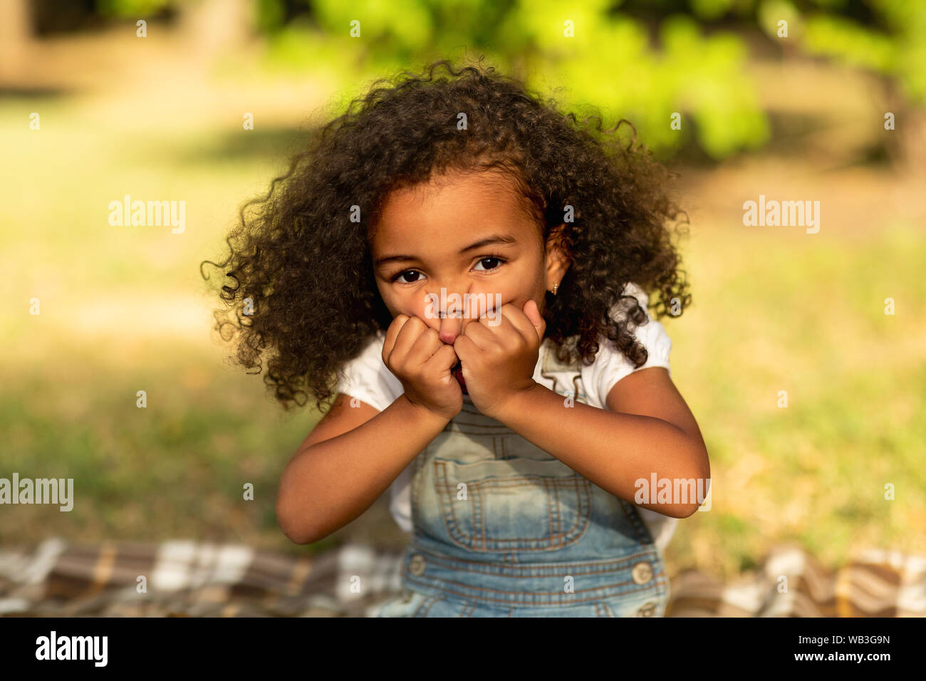 Little girl grimacing and touching cheeks in nature park Stock Photo