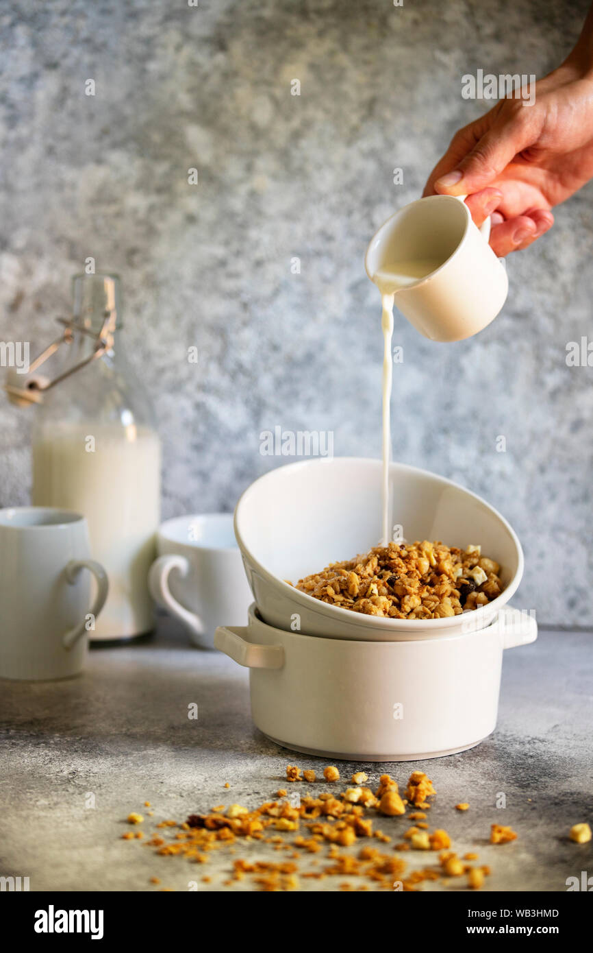 Bowl of cereal on a table, with a hand pouring milk from a glass