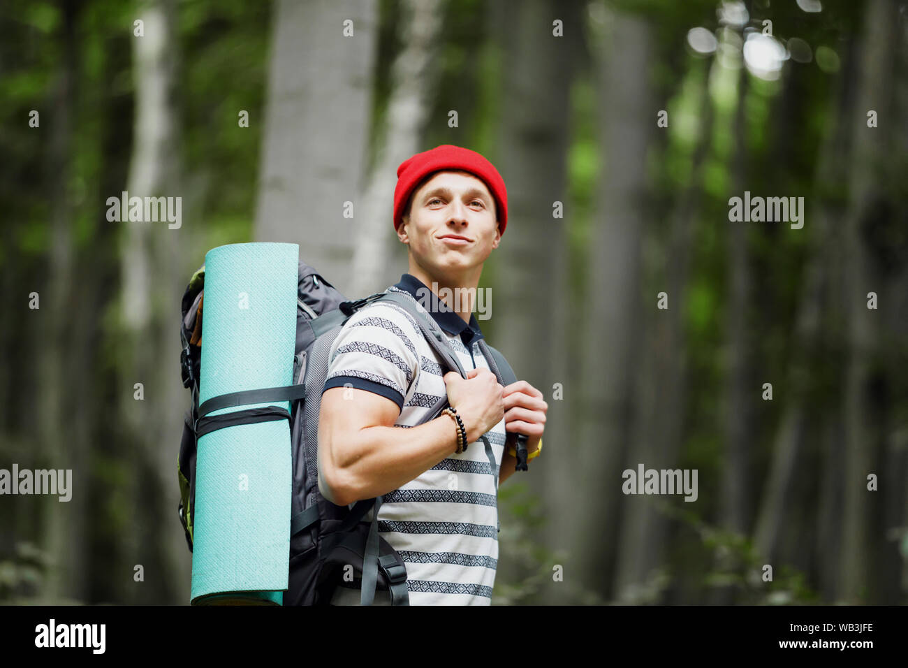 Young man wearing red hat with hiking equipment walking in mountain forest Stock Photo