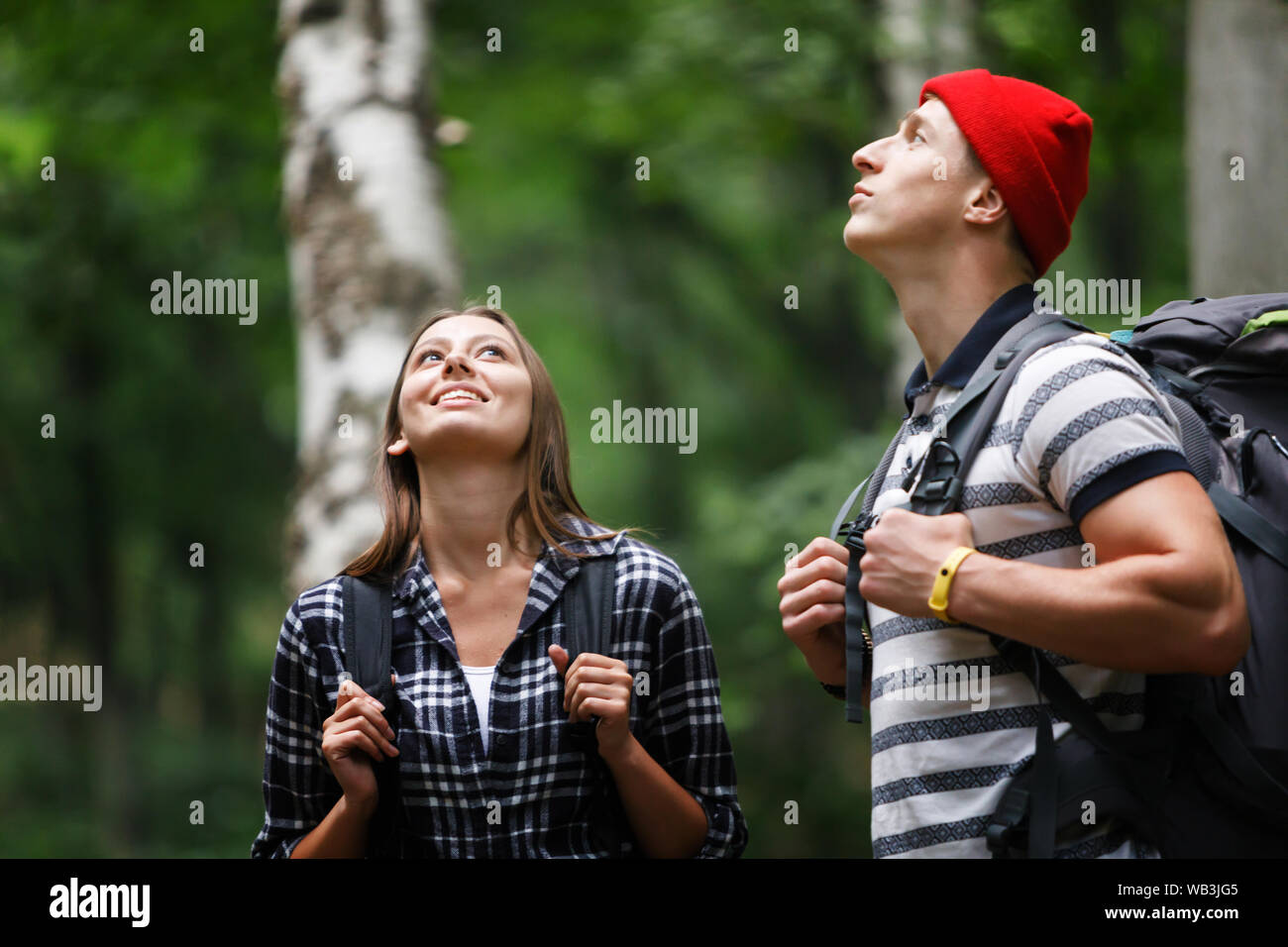 Man in red hat and woman in plaid shirt wearing backpacks in a forest expedition Stock Photo