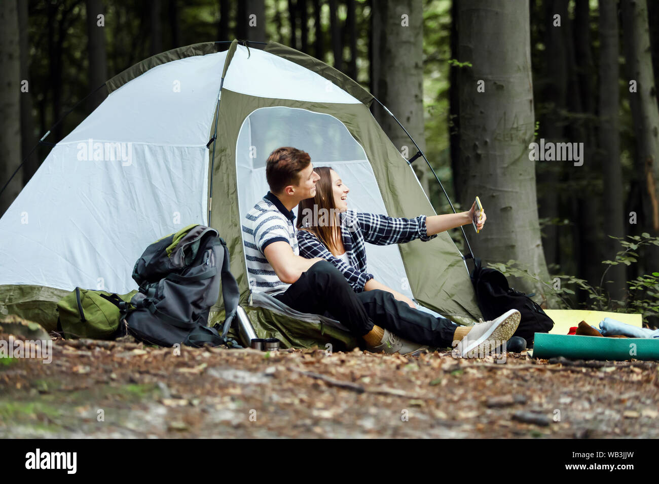 Attractive young couple resting while sitting at the tent outdoors and taking a selfie Stock Photo