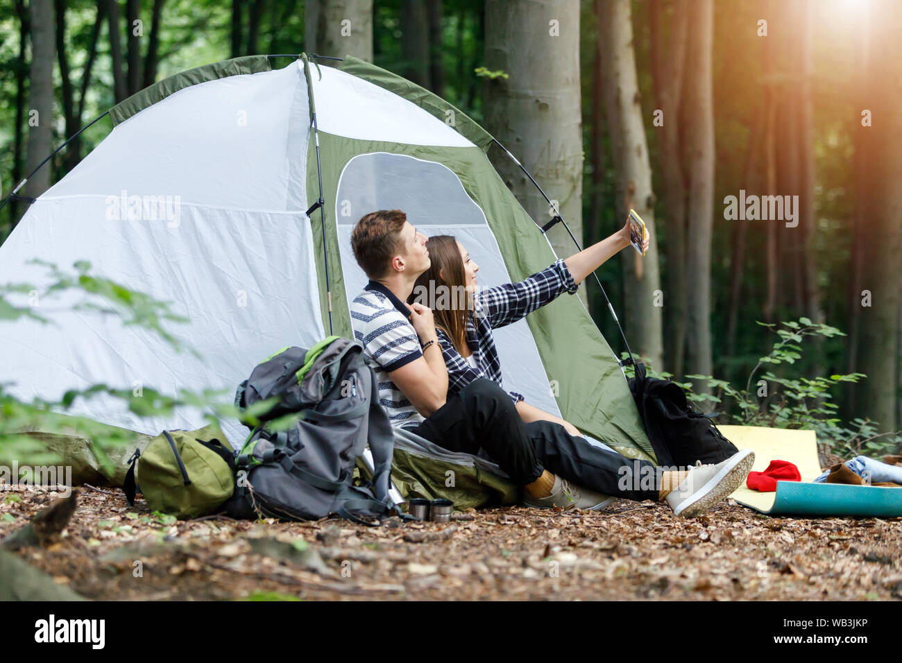 Photo of happy young loving couple outside with tent in free alternative vacation camping over mountains take selfie by mobile phone Stock Photo