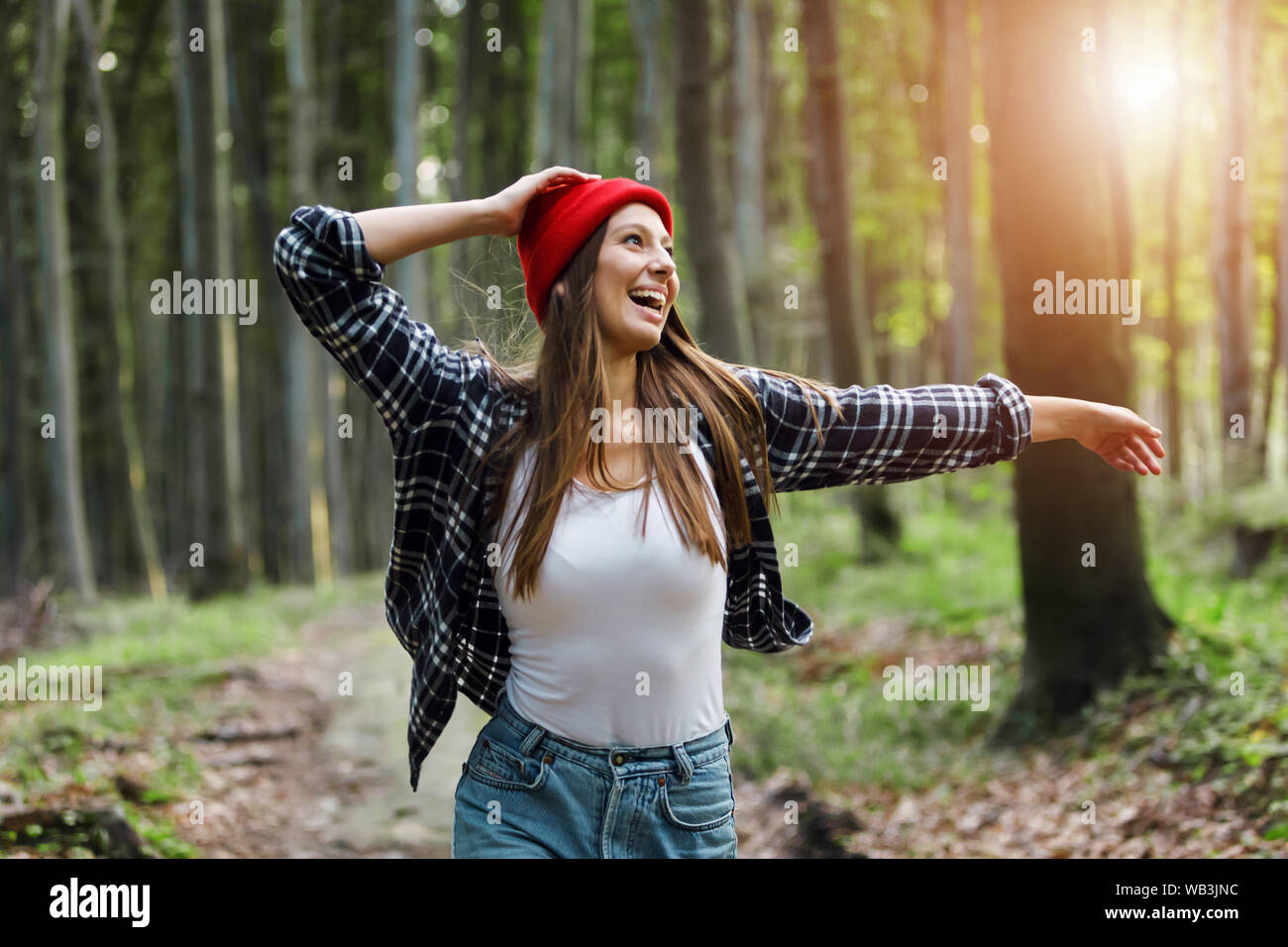 Carefree young woman dancing in forest or park and showing happiness with arms raised up Stock Photo