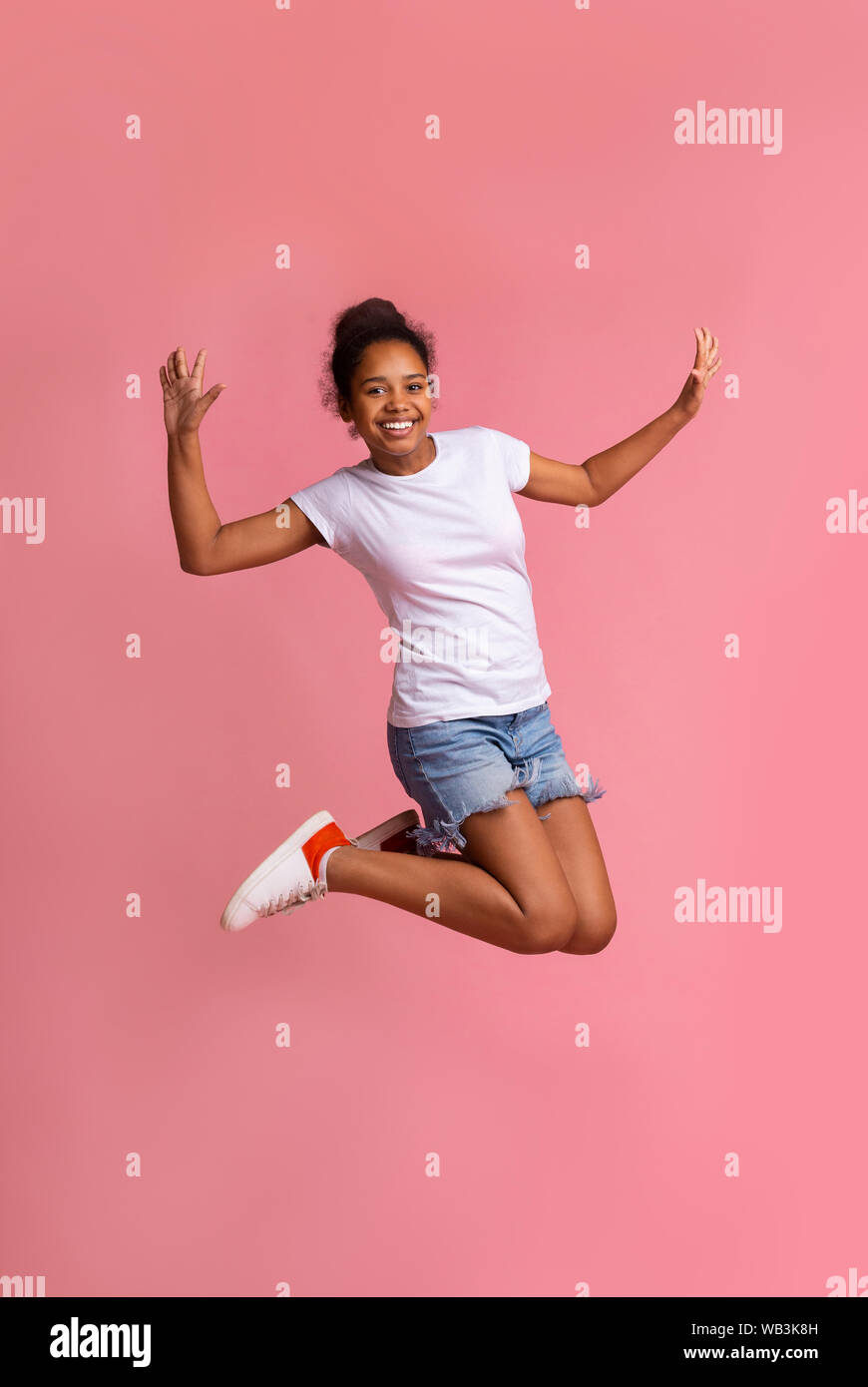 Positive african american girl jumping over pink studio background ...