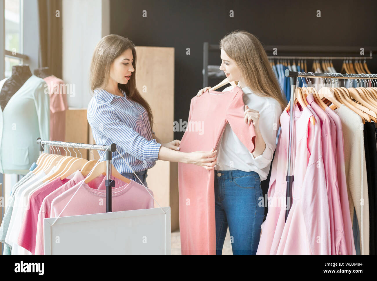 Two elegant young ladies checking on suitable dresses at boutique Stock Photo