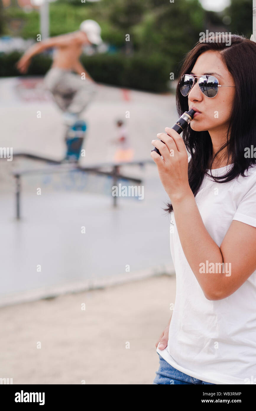 Young woman smoking with a electronic cigarette on a skateboard park Stock Photo