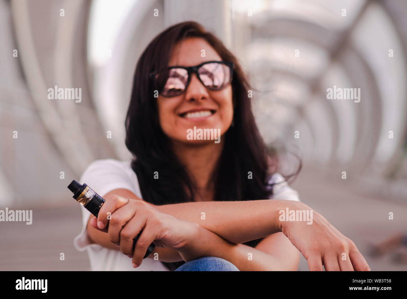 Young woman with sunglasses sitting on a picturesque bridge holding a vaper Stock Photo